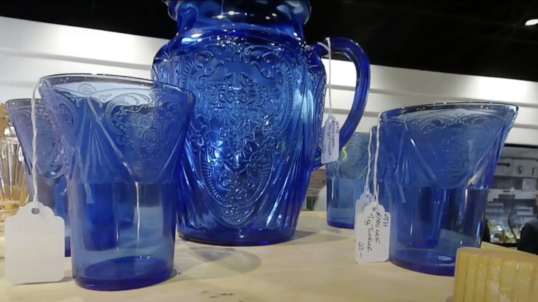 A pitcher and glasses in blue Royal Lace pattern by Hazel Atlas Glass Company sit on the shelf in a thrift store
