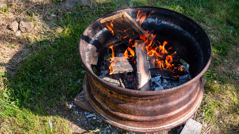 A metal vehicle wheel rim is used as a fire pit on a backyard lawn.