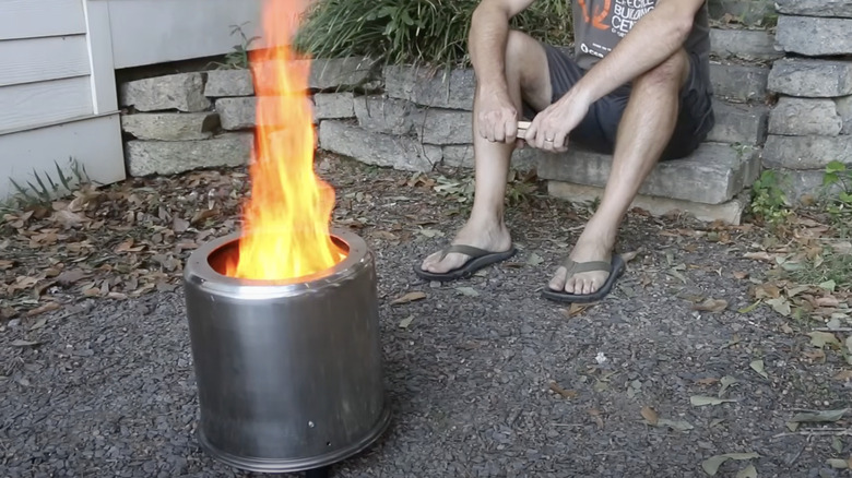 A man sits in front of a fire burning in a fire pit made from two cheap stainless steel pots.