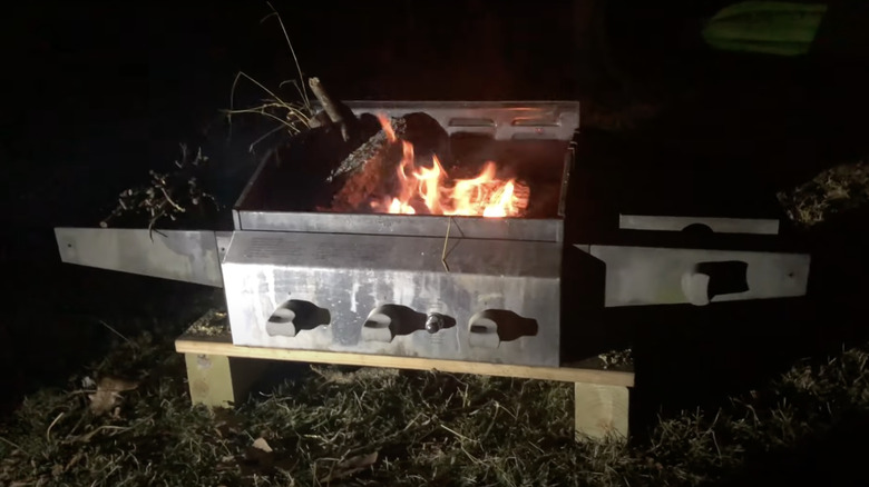 A fire burns in the middle of an old BBQ grill converted into a backyard fire pit.