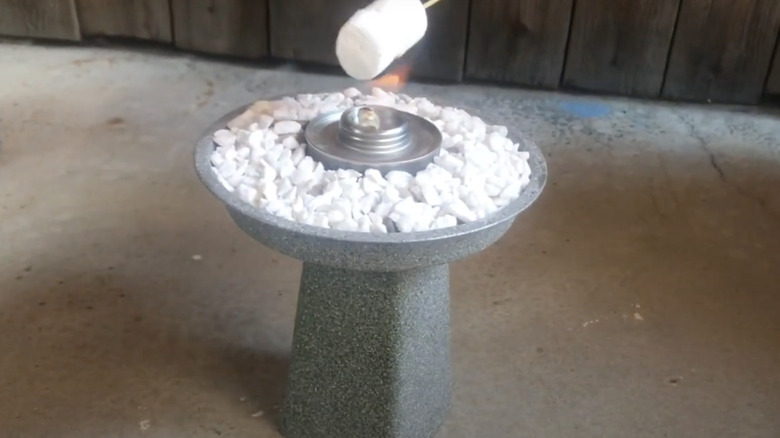 Someone toasts a marshmallow over a DIY tabletop fire pit made from a vase and a cake pan.