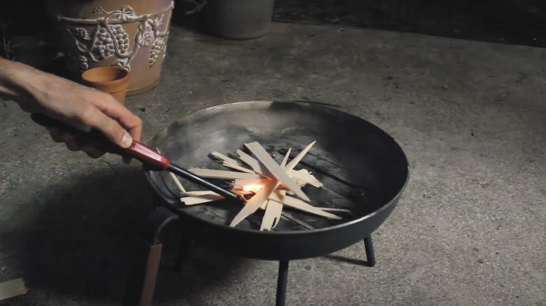 A person lights a fire in a tabletop style fire pit made from an old frying pan.
