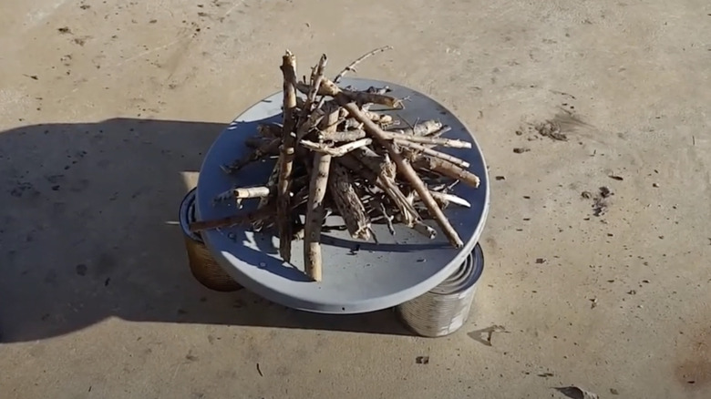 Wood ready for burning is piled atop a satellite dish held off the ground by tin cans.