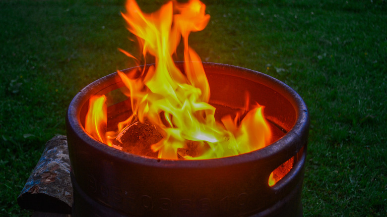 Fire burns inside an old metal barrel on a lawn.