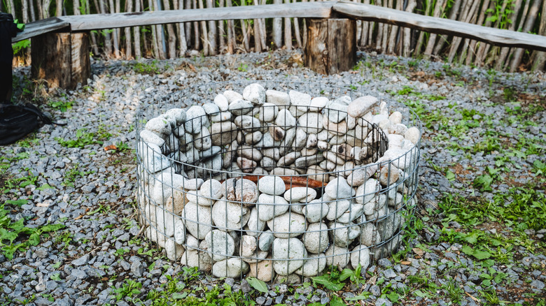 A fire pit made from large round river stones encircled by cattle panels in a gravel seating area.