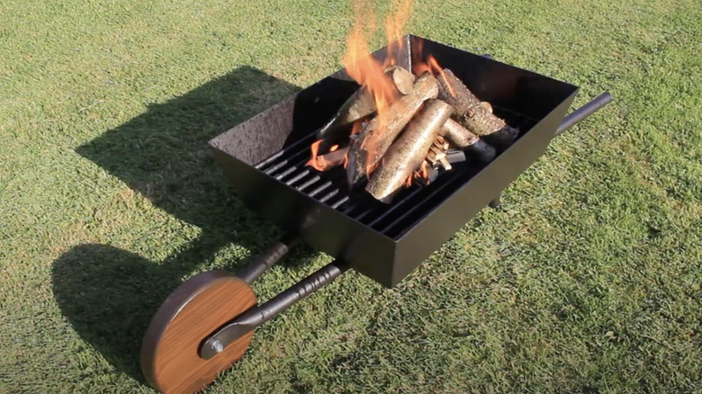A wheelbarrow repurposed into a backyard fire pit sits on a lawn.