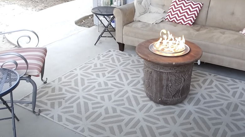 Fire burns in a fire pit made from a planter placed in the middle of an outdoor living room.