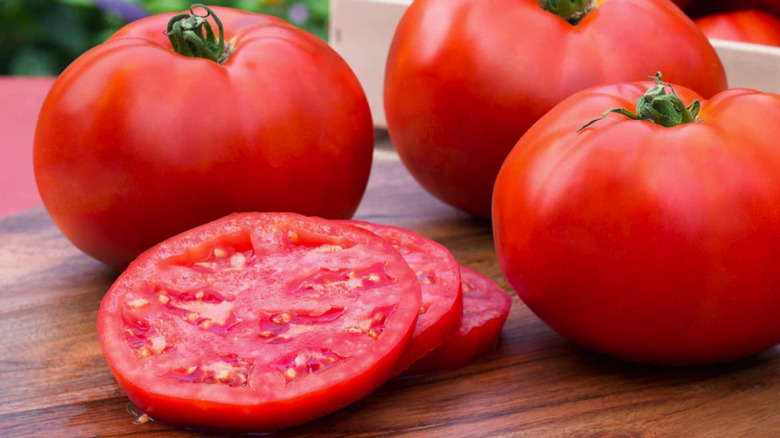 Three 'Better Boy' tomatoes sitting on a table with a three slices of tomato sitting next to them