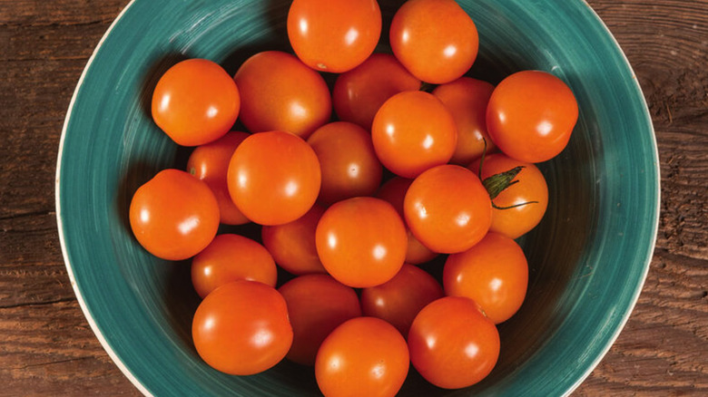A green bowl filled with orange 'Citrine Cherry' tomatoes on a wood table
