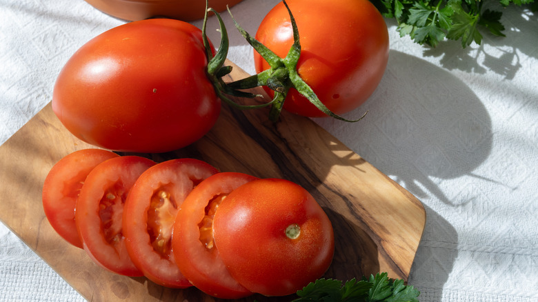Two whole 'Roma' tomatoes on a cutting board with one sliced