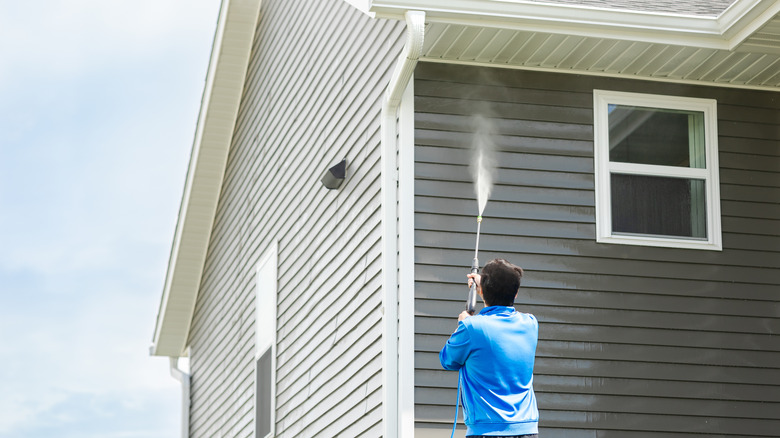 Man pressure washing house