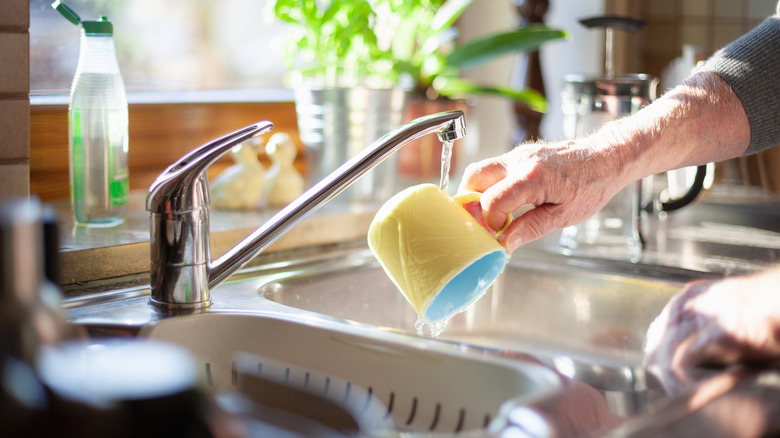 A person washing a yellow mug with a blue interior in a sink