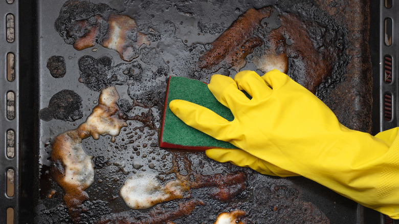 Person with a gloved hand cleaning a greasy baking sheet