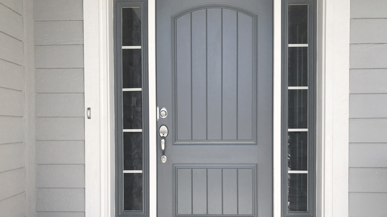 A cement gray door is surrounded by white trim and light gray siding