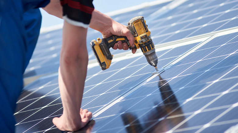 man drilling solar panel to roof