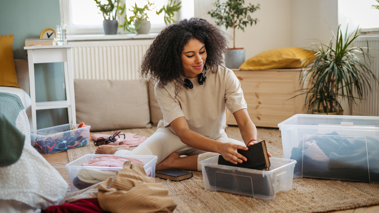 Woman sorting through items in plastic bins on floor of living area
