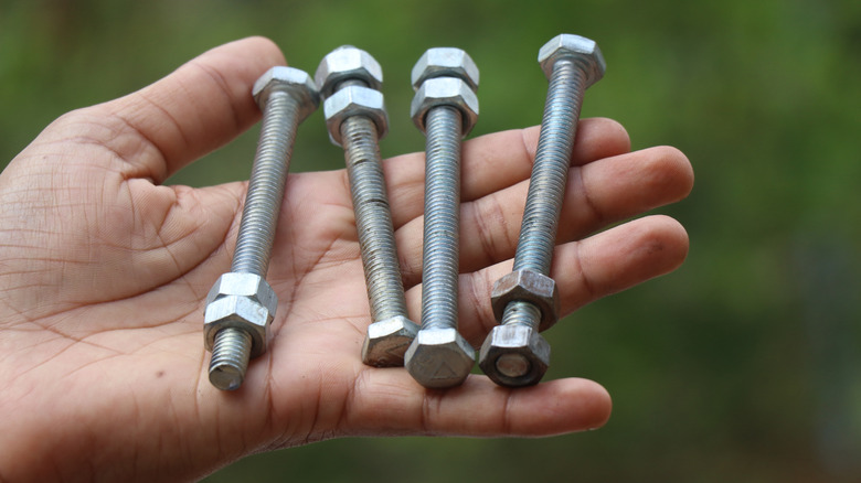 A hand holds four bolts with two nuts on each