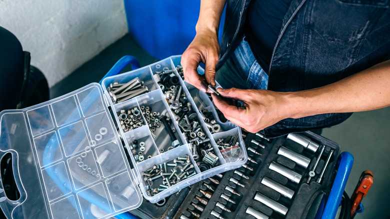 A person chooses an item from a box of nuts and bolts