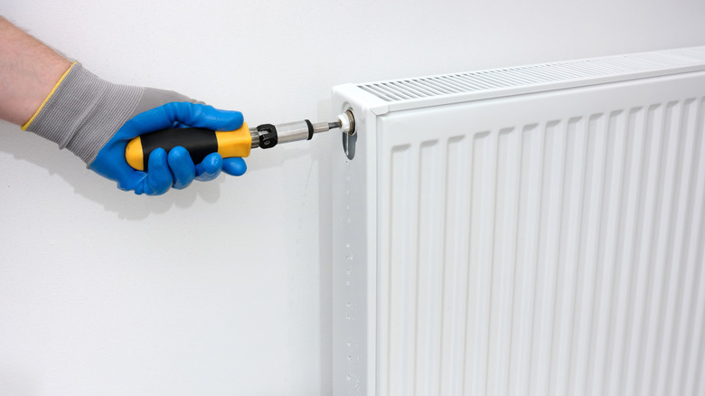 A person wearing gloves bleeds a radiator with tool.