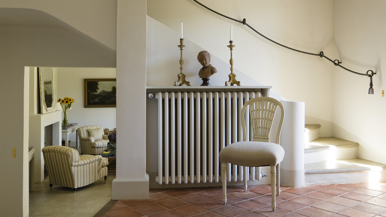 A radiator in a stairwell with decorations on a shelf above it and a chair in front of it.