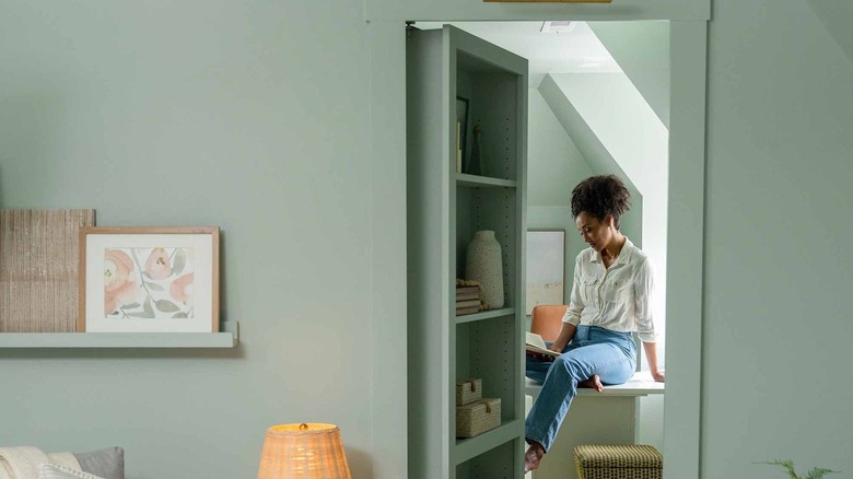 A woman sitting on a table in a room hidden by a bookshelf Murphy door.