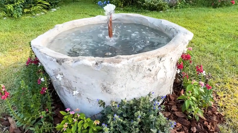 Gray water fountain with flowers around it.