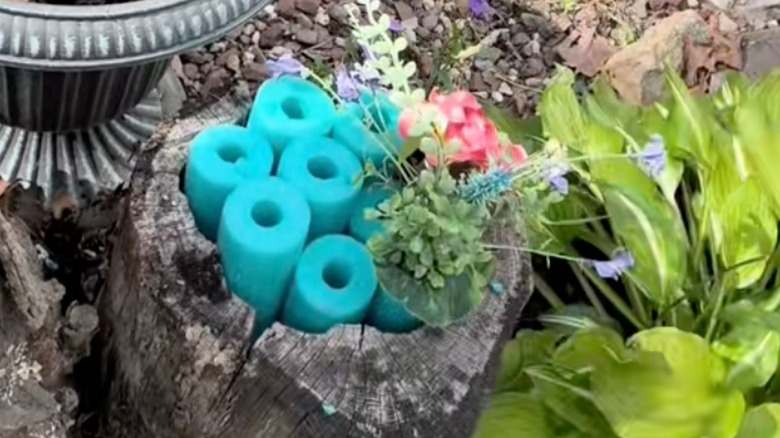 Blue pool noodles and flowers in tree stump.