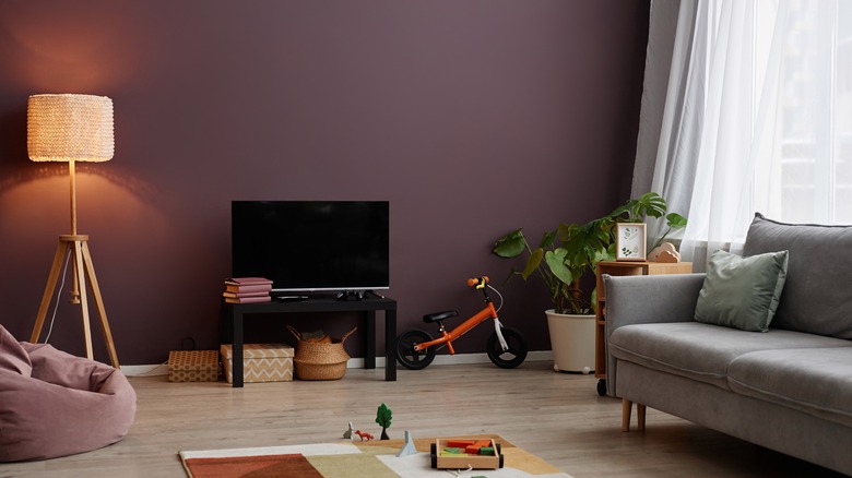 A mauve living room with couch, lamp, tv, and window.