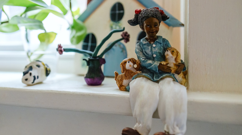 Porcelain figurine of girl and dogs sitting on window sill.