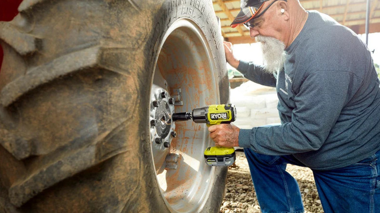 A man using the Ryobi ONE+ 18V Impact Wrench to remove lugnuts from a tractor tire