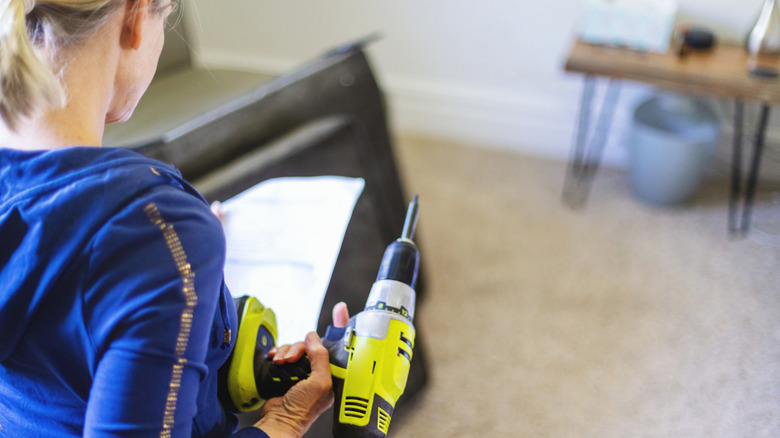Woman holding a Ryobi drill and looking at a piece of paper in a living room