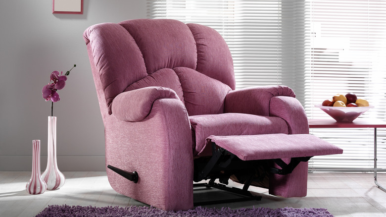 A magenta recliner in a living room adorned with vases, flowers, and fruits.