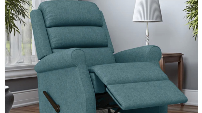 A blue recliner with its leg rest up featured in a living room with plants, a side table with a lamp, and wooden flooring.