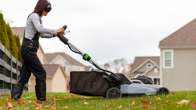 A woman is using a walk-behind mulching mower in her yard
