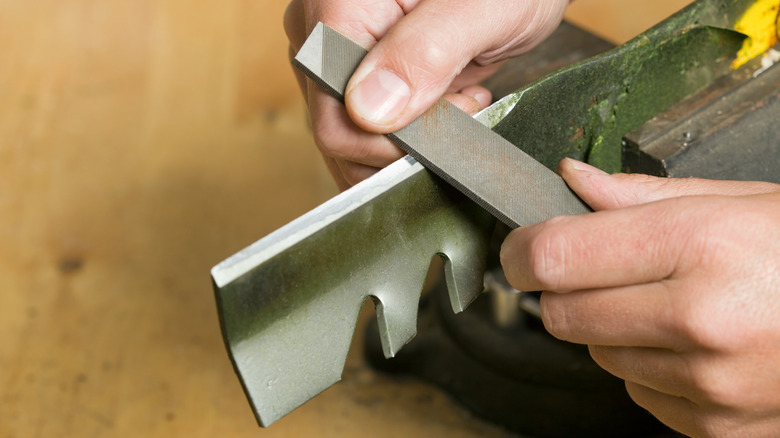 Male hands sharpening a mulching mower blade with a metal file
