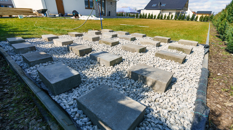 A foundation of landscape fabric, gravel, and concrete blocks for a backyard shed.
