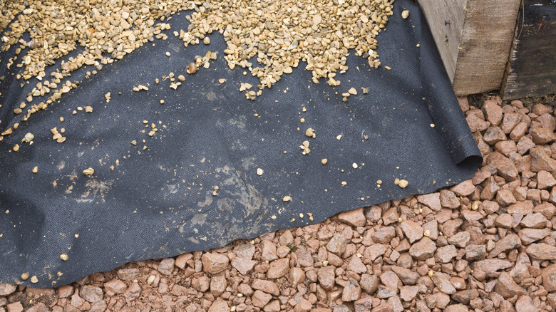 A red gravel garden path with a sheet of black landscape fabric and more small white gravel on it.
