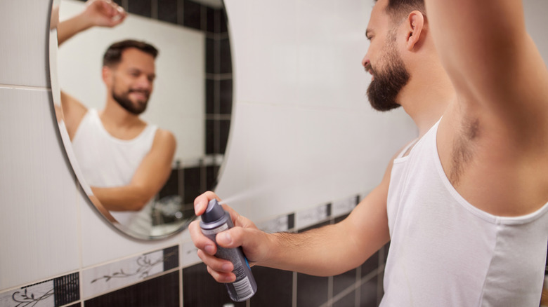 man using aerosol deodorant in front of a bathroom mirror
