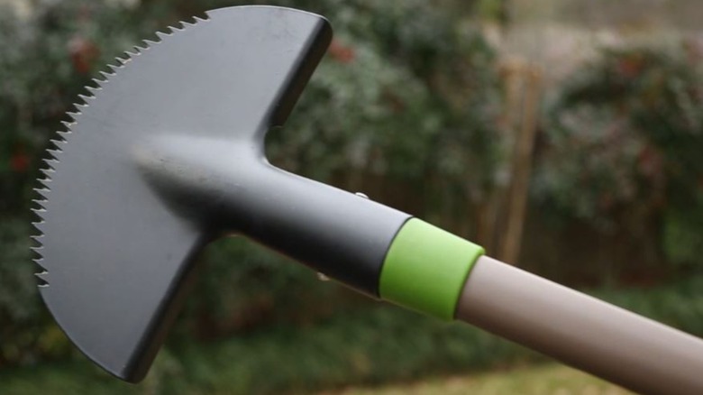 An Ames border edger held in the air against a blurred backdrop of shrubs and trees in a garden.