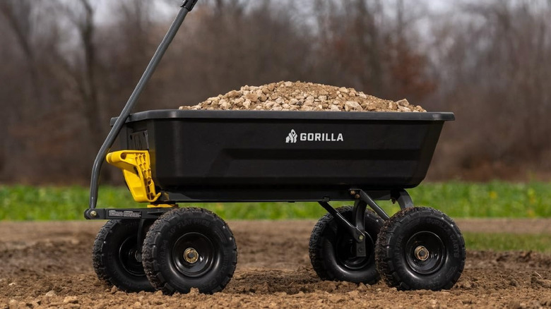 A black Gorilla Cart filled with gravel sits on a gravel driveway.