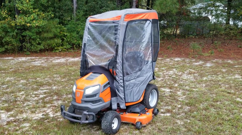 An orange riding mower with a temporary cab.