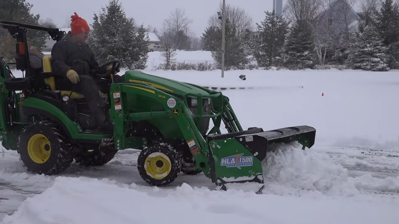 A man using a large lawn mower tractor with a snow pusher/box.