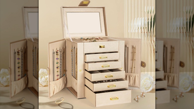 A white AKOZLIN jewelry box opened with rings, necklaces, and bracelets inside its open drawers