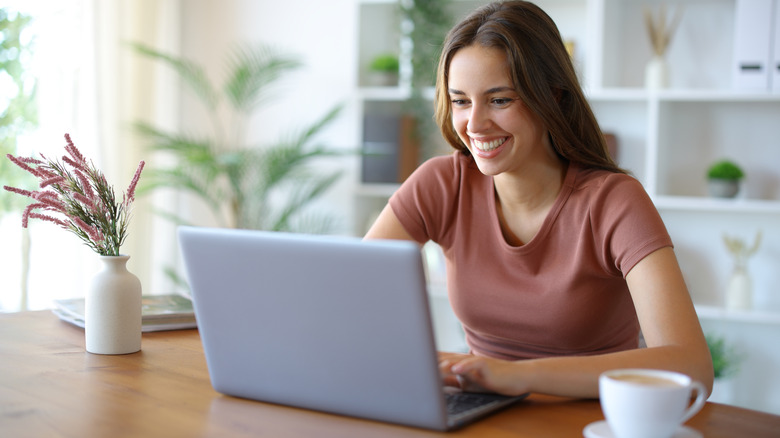 Young woman in a pink shirt typing on a silver laptop at home