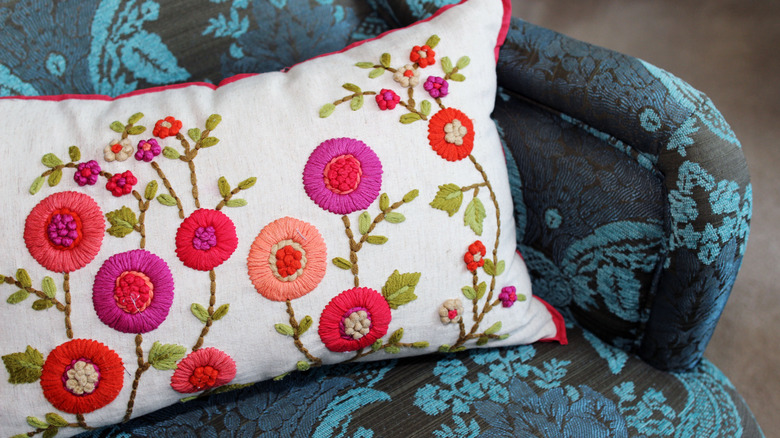 An embroidered pillow with flowers on it sitting on a damask armchair.