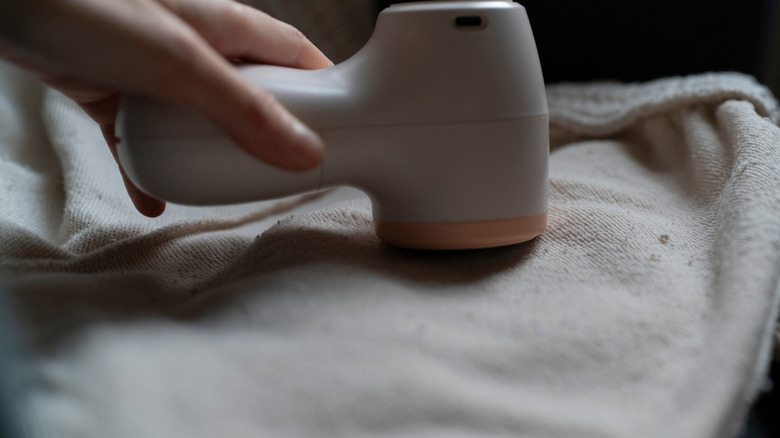 A hand applying a fabric shaver to a blanket.