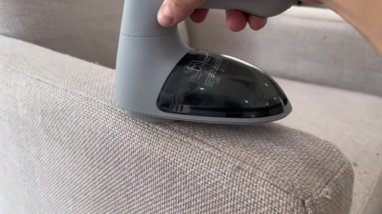 A sweater shaver being used on a couch arm.