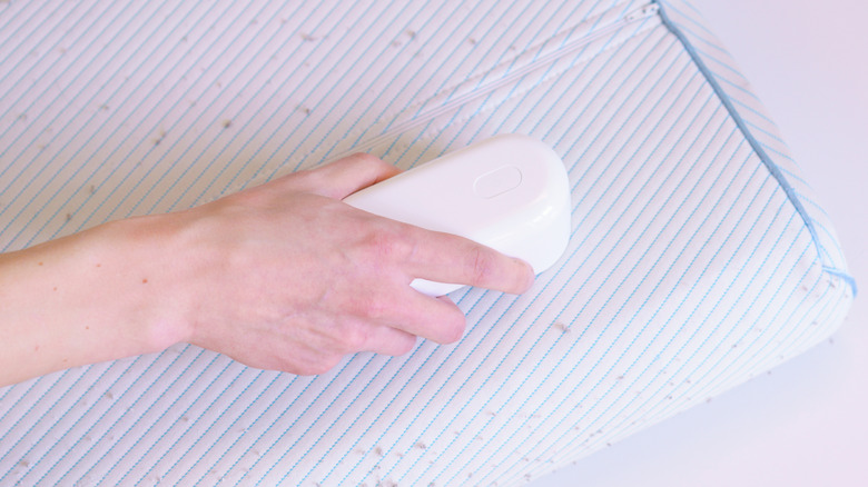 A hand using a fabric shaver on a pillow.