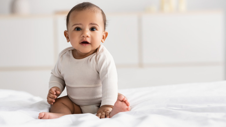 baby sitting on white mattress