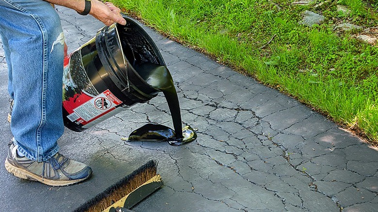 A person pouring a sealant on an asphalt driveway